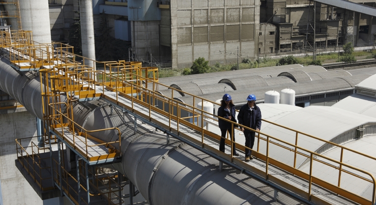 2 people walking at cement plant, pipes, height